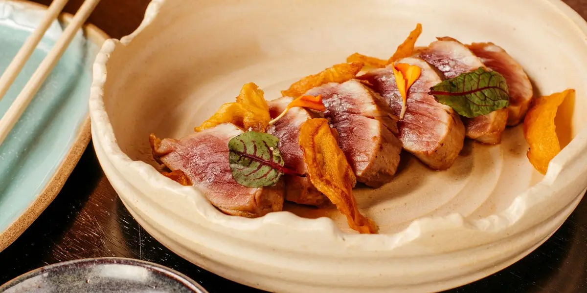 Magret de canard doré dans une poêle, peau croustillante et chair rosée tranchée sur une planche.