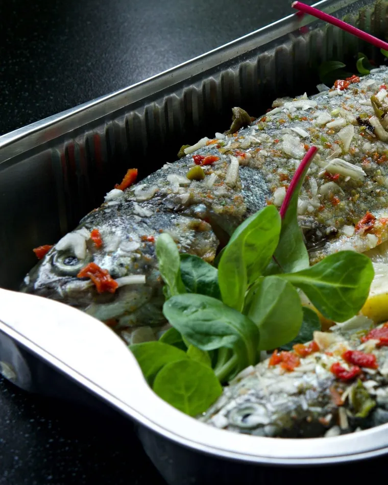 Truite entière cuite au four dans son plat, aromates, mâche et citron